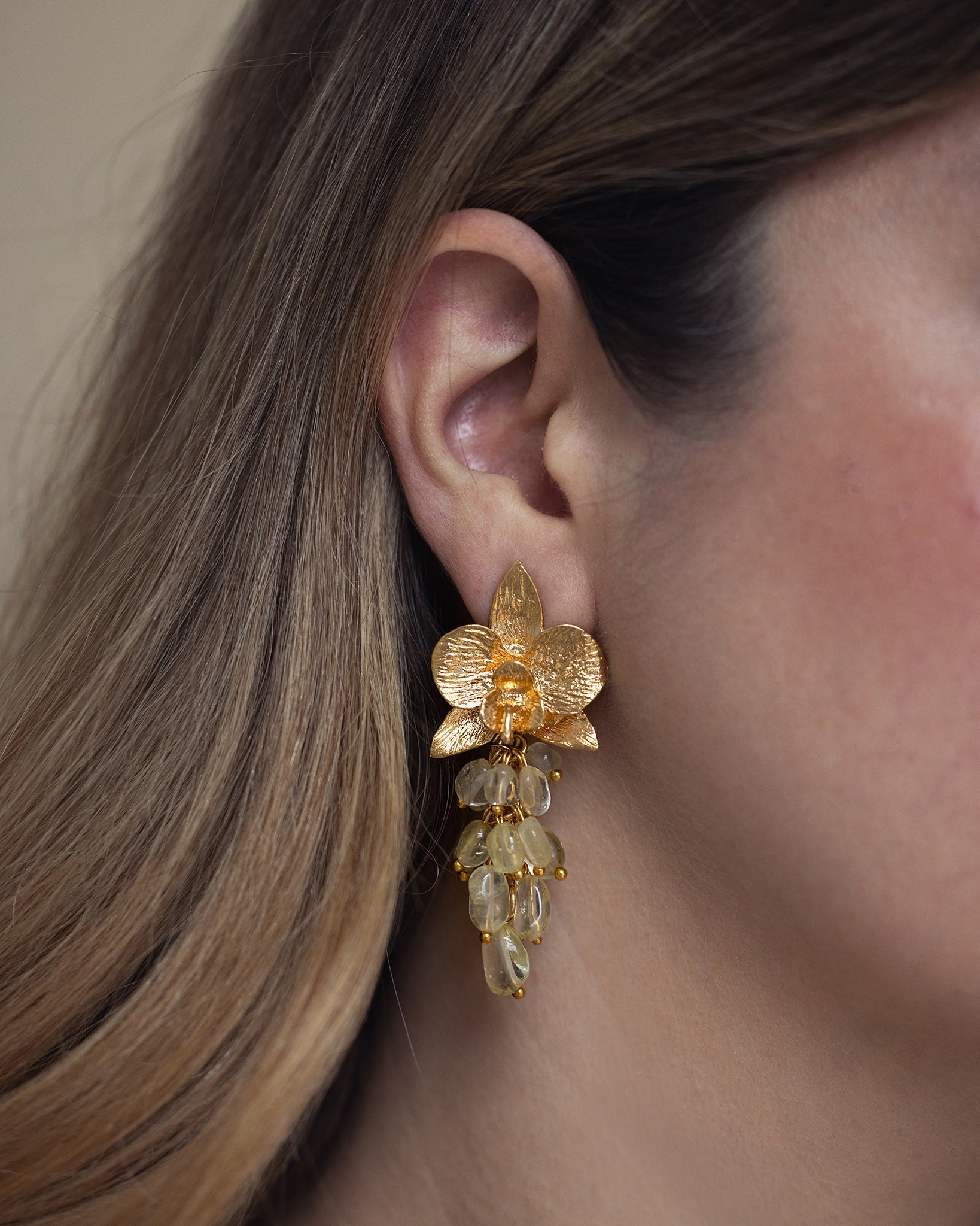 Woman wearing citrine orchid statement earrings with golden floral details