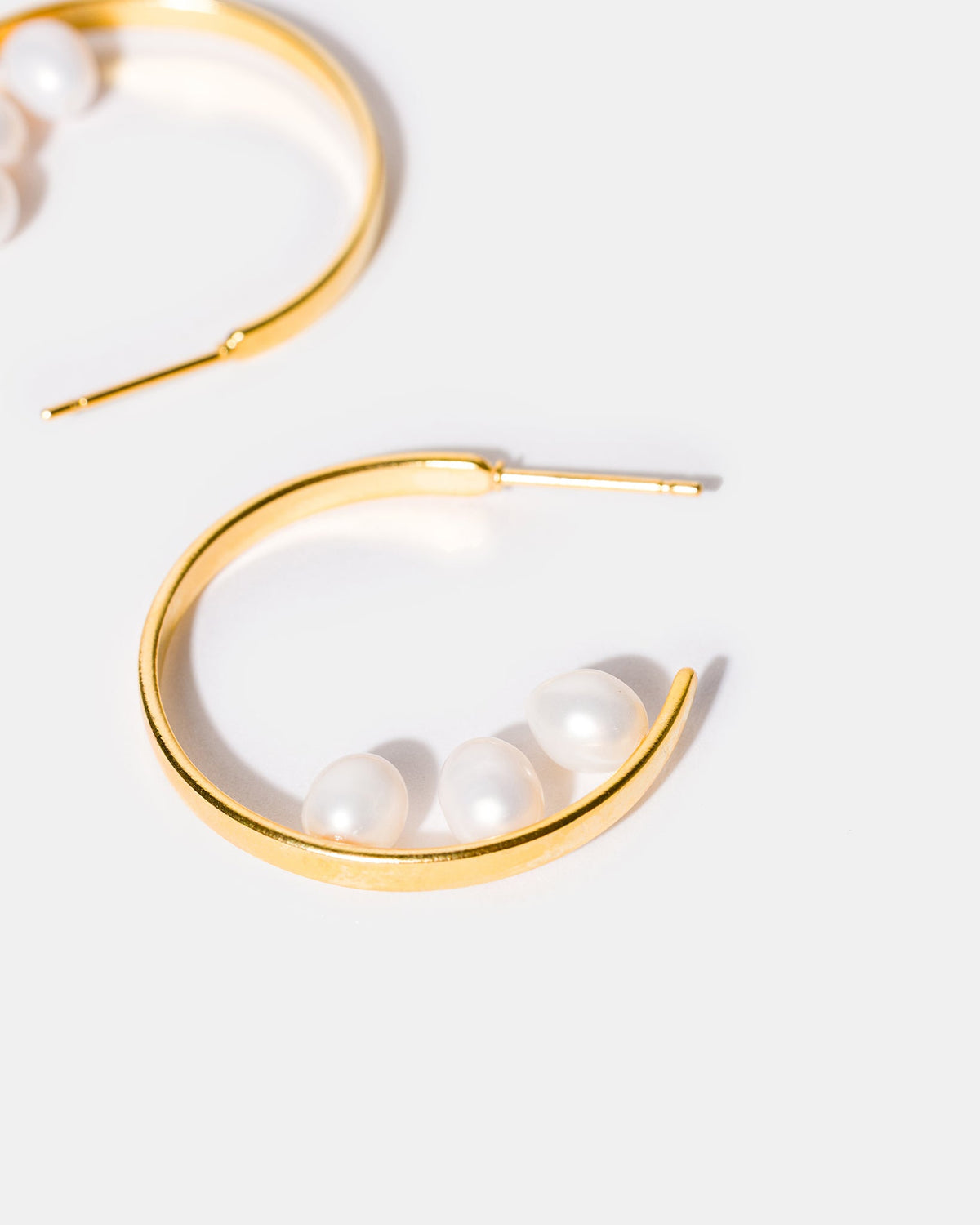 Close-up detail of freshwater pearl inside-out hoop earrings showing gold-plated curved design