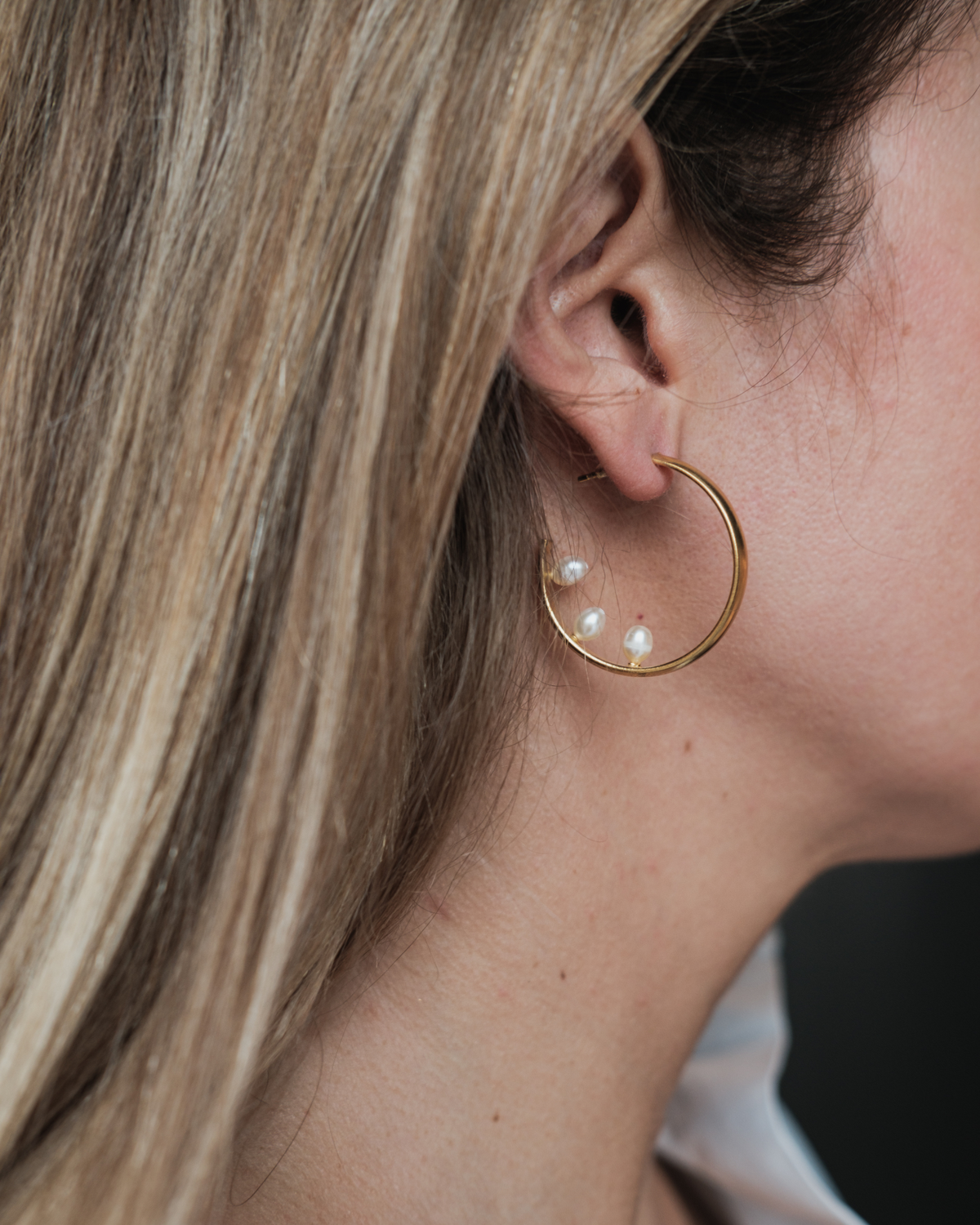 Woman wearing freshwater pearl inside-out gold hoop earrings in a minimal everyday look