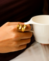 Gold sculptural ring worn while holding a cup